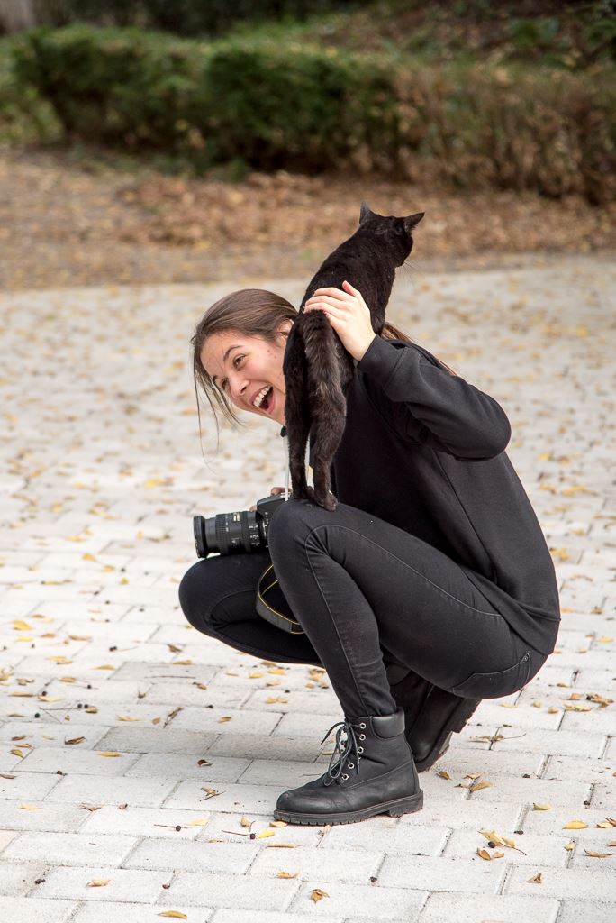 photo of Matea (me) crounching and laughing while a cat is standing on my leg and shoulder